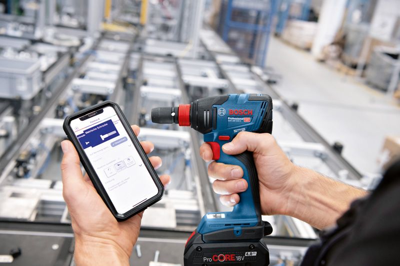 한 사람이 산업 현장에서 무선 드릴을 제어하기 위해 스마트폰을 사용하고 있습니다.