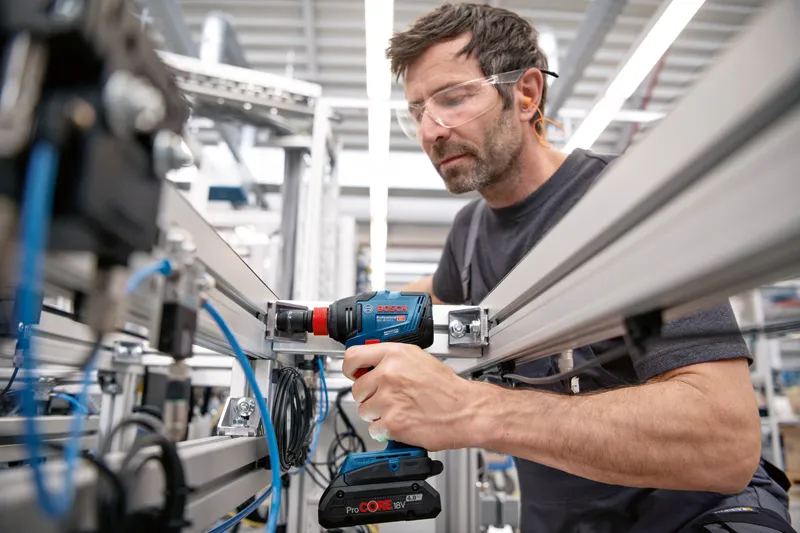 안전장비를 착용한 사람이 무선 드릴을 사용하여 금속 프레임을 고정합니다.