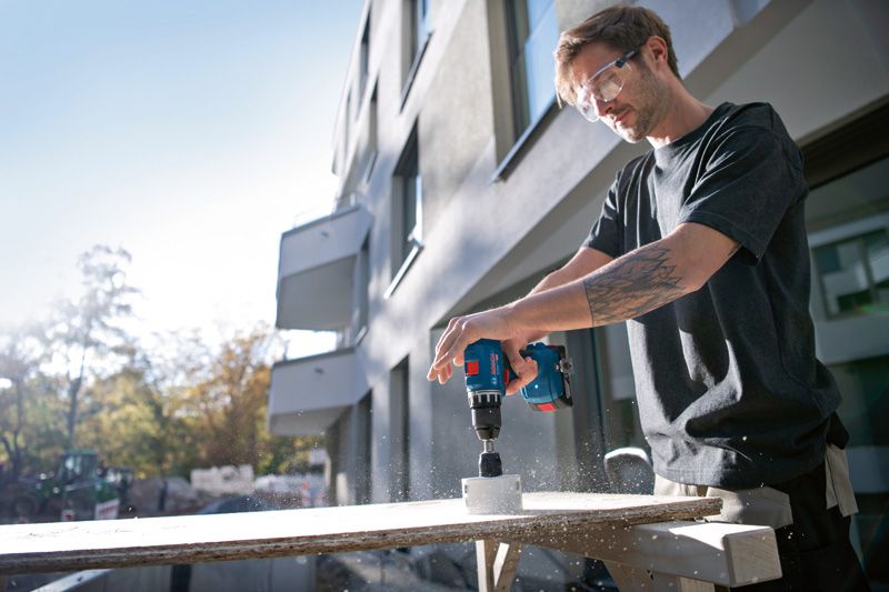 안전장비를 착용한 사람이 야외에서 전동 드릴을 이용해 나무에 구멍을 뚫고 있습니다.