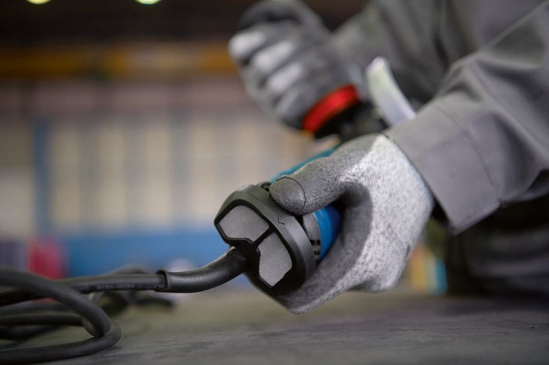 안전 장비를 착용한 사람이 작업대 위에 전선이 있는 전동 공구를 잡고 있습니다.