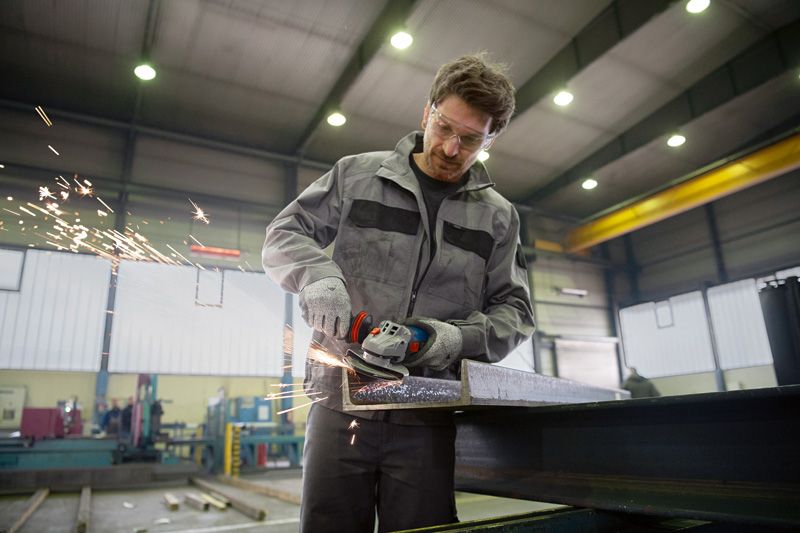 안전장비를 착용한 사람이 강철 빔을 갈아서 튀는 불꽃을 발생시킨다.