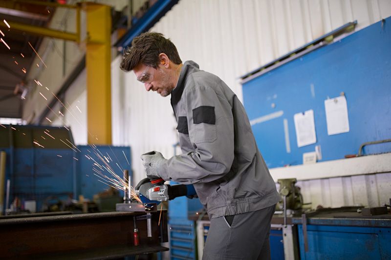 안전 장비를 착용한 사람이 작업장에서 금속을 갈아서 불꽃이 튀는 모습입니다.