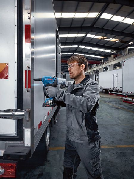 안전장비를 착용한 사람이 무선 리벳 건을 이용해 트럭 문을 뚫고 있습니다.