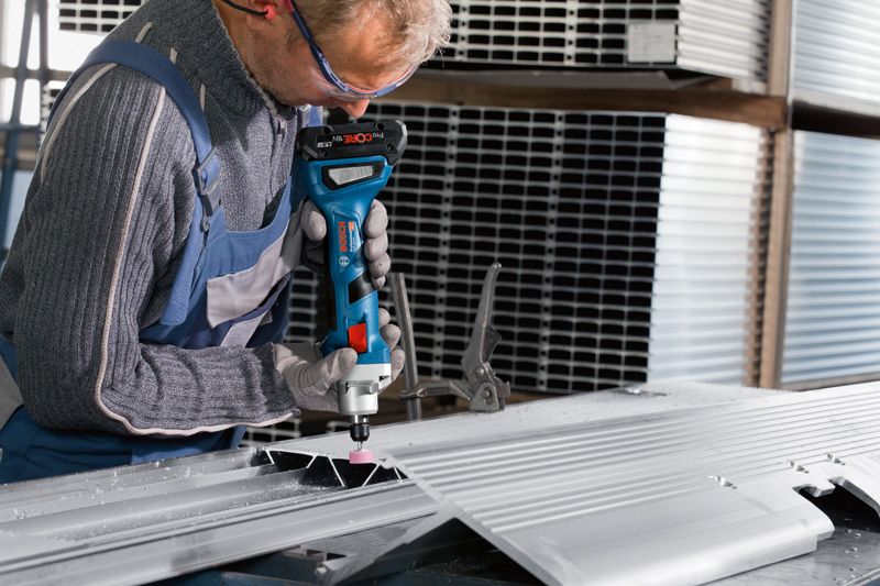 안전 장비를 착용한 사람이 무선 스트레이트 그라인더로 금속판을 갈고 있습니다.