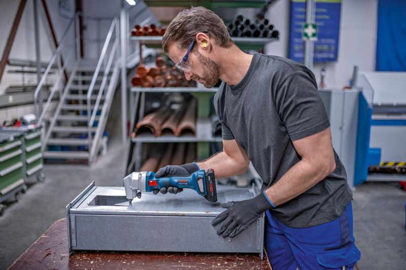 안전장비를 착용한 사람이 무선 니블러로 금속판을 다듬고 있습니다.