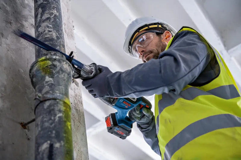 안전장비를 착용한 사람이 왕복톱으로 파이프를 자릅니다.