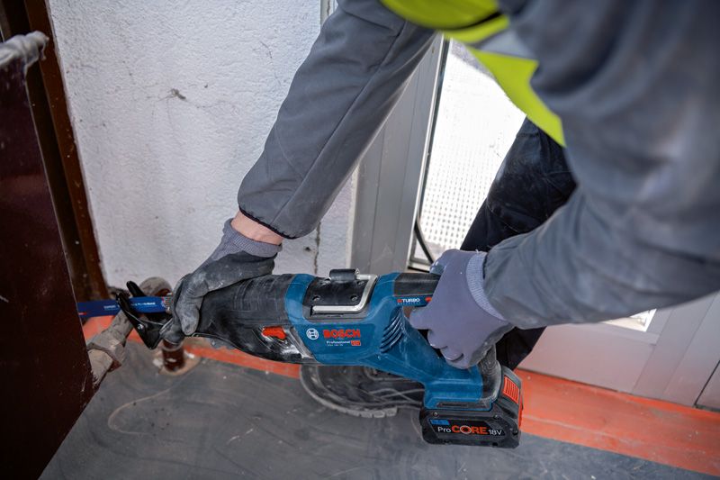 안전 장비를 착용한 사람이 무선 왕복톱을 사용하여 금속을 절단하고 있습니다.