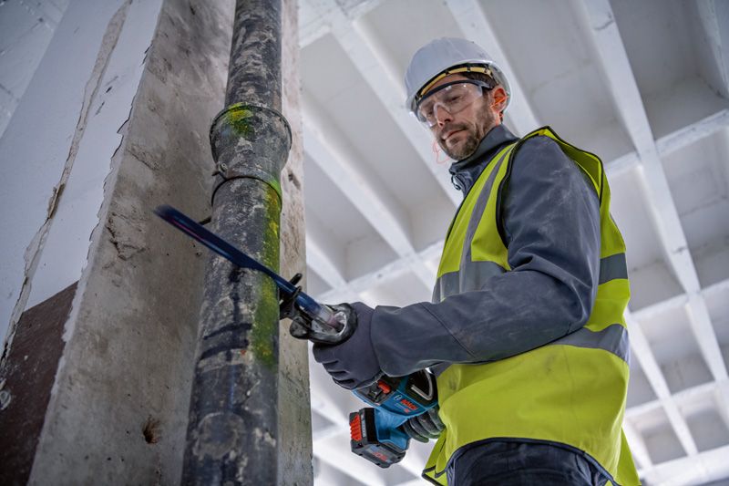 안전장비를 착용한 사람이 왕복톱으로 금속 파이프를 자릅니다.