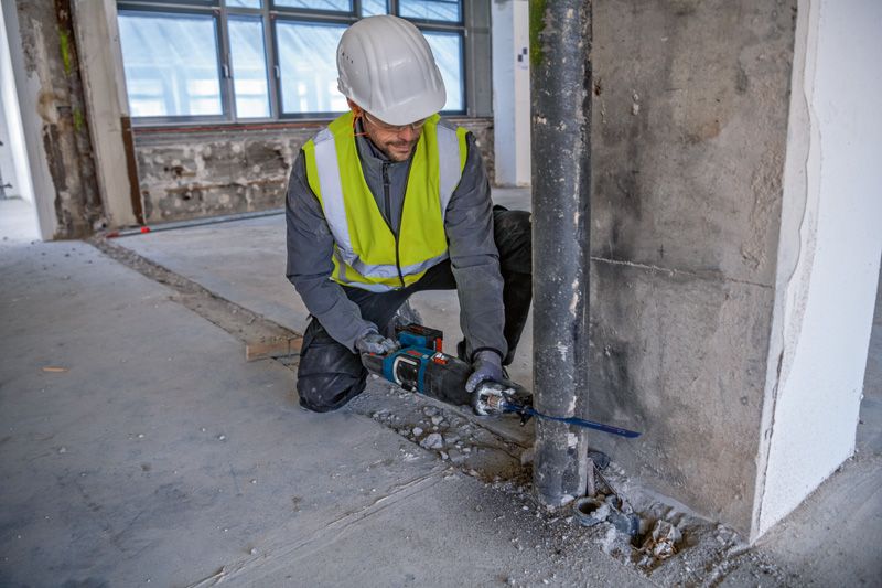 안전 장비를 착용한 사람이 왕복톱을 사용해 금속 파이프를 자릅니다.