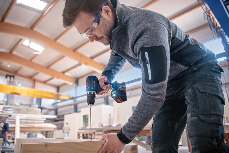 안전장비를 착용한 사람이 무선 전동공구를 이용해 나무에 구멍을 뚫고 있습니다.
