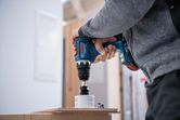 한 사람이 무선 드릴로 나무에 구멍을 뚫고 있다.