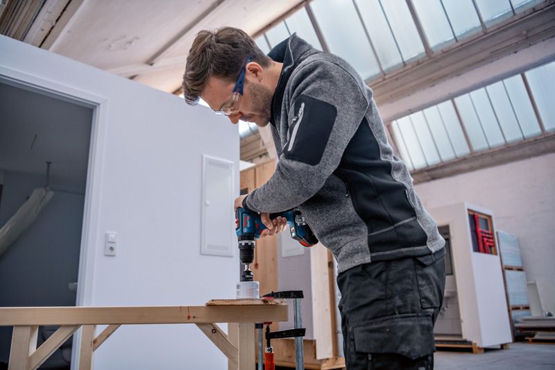 안전장비를 착용한 사람이 무선 전동 드릴을 사용하여 나무에 구멍을 뚫고 있습니다.