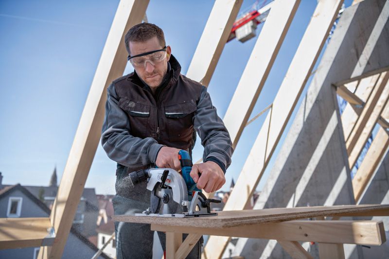 안전 장비를 착용한 사람이 건설 현장에서 원형 톱을 사용하여 합판을 자르고 있습니다.