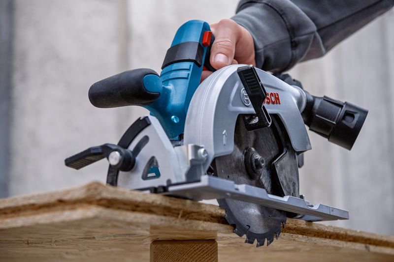 한 사람이 건설 현장에서 원형 톱으로 나무를 자르고 있다.