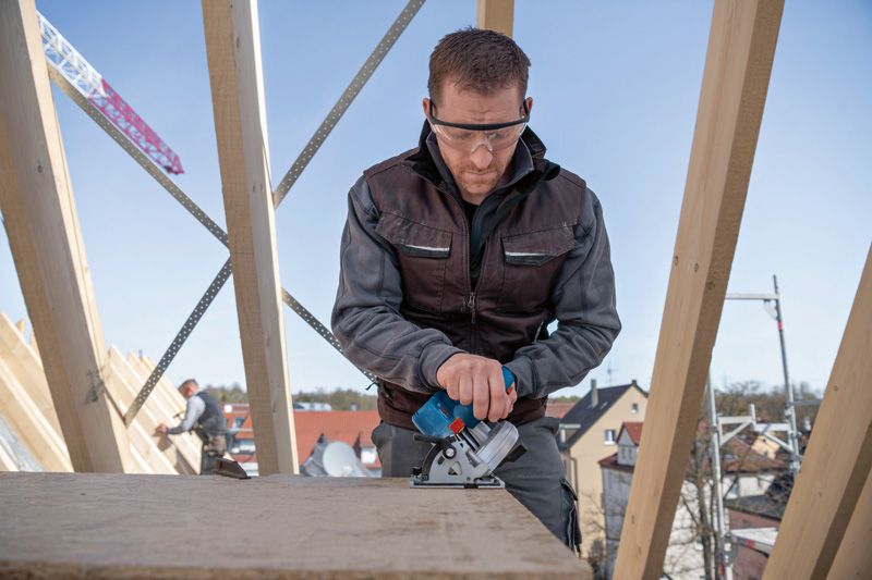 안전 장비를 착용한 사람이 건설 현장에서 전기톱을 사용하여 나무를 자릅니다.