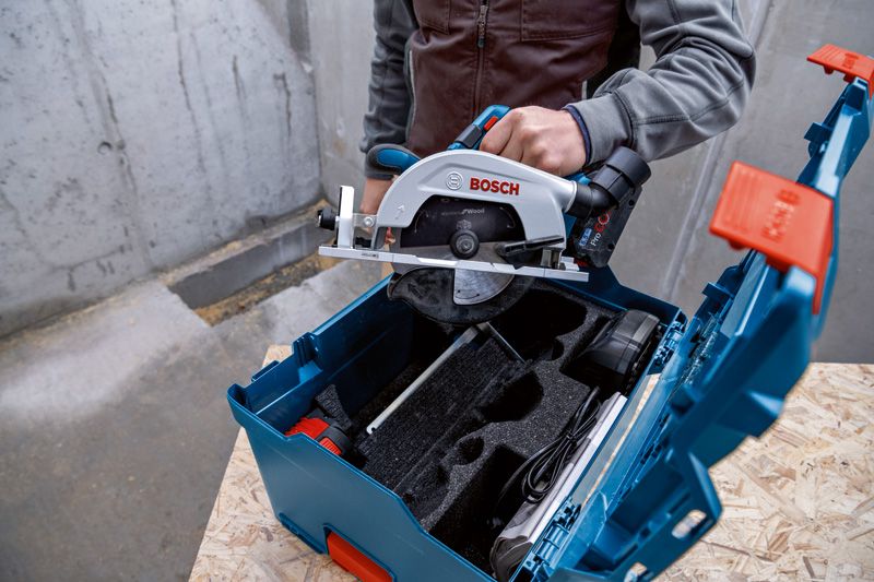 한 사람이 나무 표면 위의 파란색 도구 상자에 원형 톱을 넣고 있습니다.