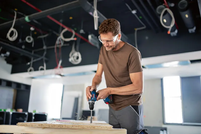 안전장비를 착용한 사람이 건설 현장에서 패널에 구멍을 뚫고 있습니다.
