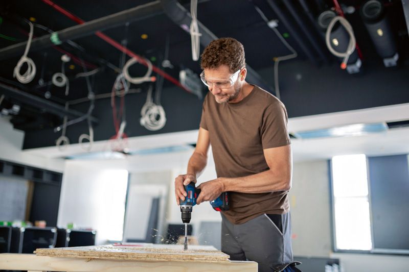 안전장비를 착용한 사람이 건설 현장에서 패널에 구멍을 뚫고 있습니다.