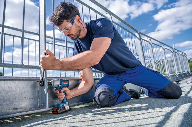 안전 장비를 착용한 사람이 무선 충격 렌치를 이용해 금속 울타리를 고정하고 있습니다.