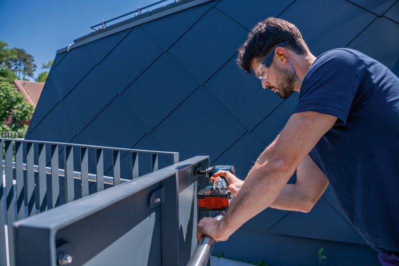 GDS 18V-330 HC 안전장비를 착용한 사람이 실외에서 금속 난간에 구멍을 뚫고 있습니다.