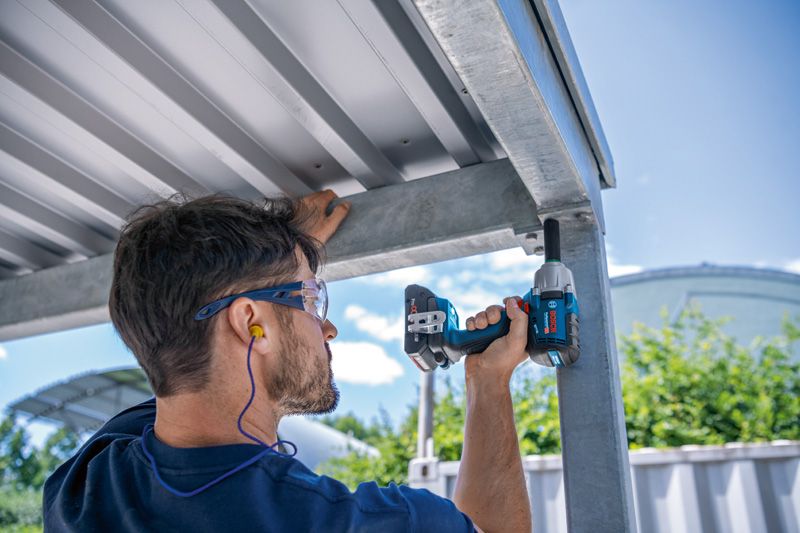 안전장비를 착용한 사람이 금속 구조물에 충격 렌치를 사용하고 있습니다.