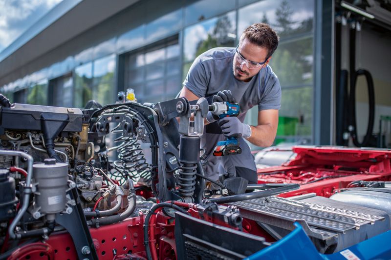 안전 장비를 착용한 사람이 차량 섀시에 무선 충격 렌치를 사용하고 있습니다.