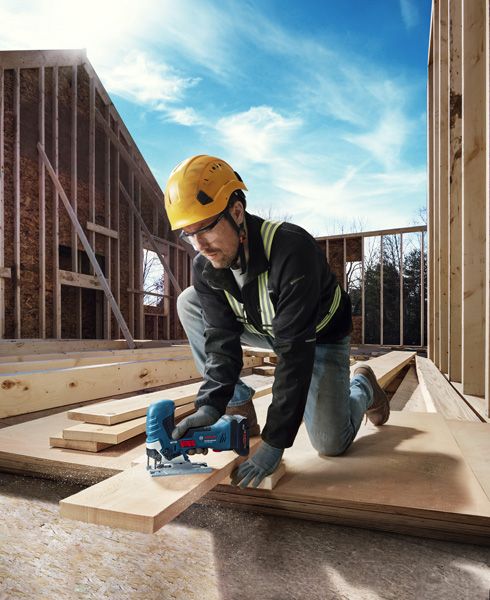 GST 18V-125 S 안전 장비를 착용한 사람이 건설 현장에서 톱으로 합판을 자르고 있습니다.