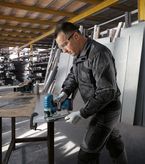 안전 장비를 착용한 사람이 작업장에서 무선 톱으로 금속판을 자르고 있습니다.