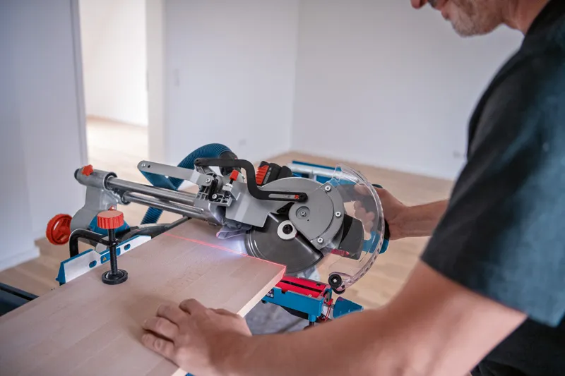 한 사람이 레이저 레벨링 도구가 달린 무선 마이터 톱을 사용해 나무를 자릅니다.