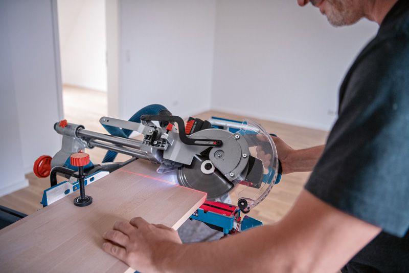 한 사람이 레이저 수평 조절 장치가 장착된 무선 각도 절단기를 사용하여 나무를 자르고 있습니다.