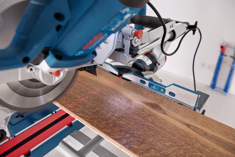 레이저 레벨링 도구가 장착된 마이터 톱으로 작업대 위의 나무 판자를 자르고 있습니다.