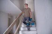 미완성 건물 내부의 계단 위로 한 사람이 모서리톱을 들고 올라가고 있다.