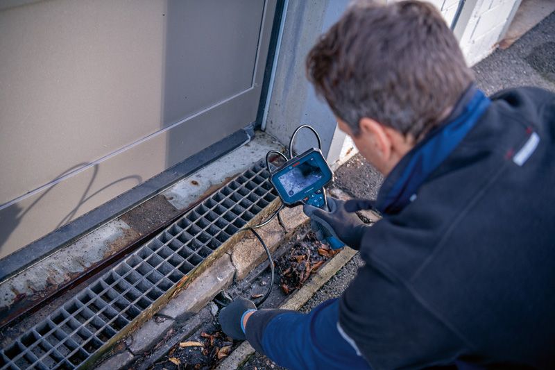 안전 장비를 착용한 사람이 검사 카메라로 배수구를 검사하고 있습니다.