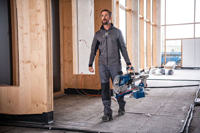 안전 장비를 착용한 사람이 건설 현장에서 무선 각도절단기를 들고 있다.