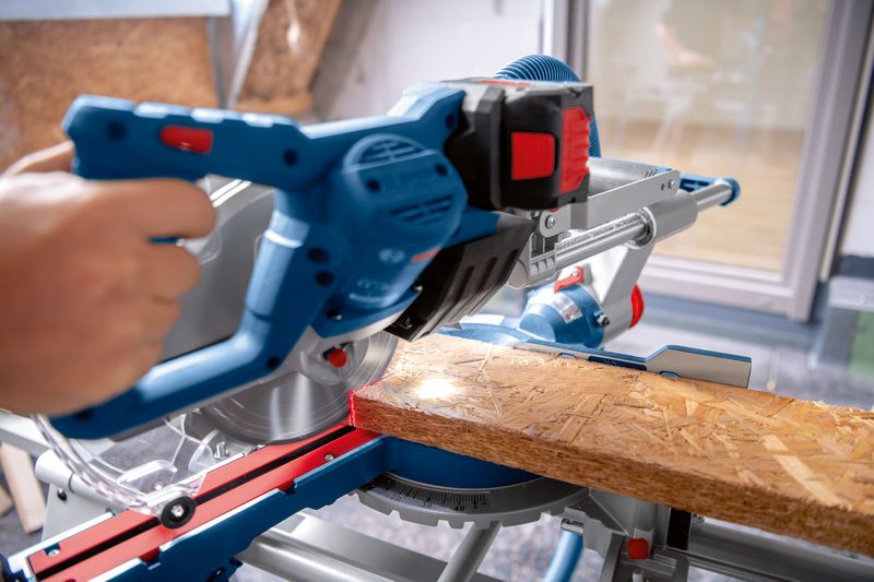 사람이 작업대 위에 있는 무선 마이터 톱으로 나무판을 자르고 있습니다.