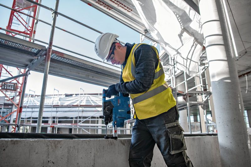 안전장비를 착용한 사람이 건설 현장에서 콘크리트에 구멍을 뚫고 있다.