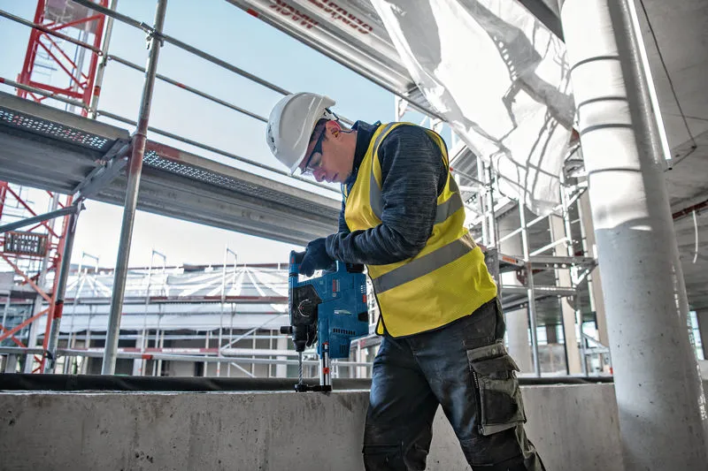 안전장비를 착용한 사람이 건설 현장에서 콘크리트에 구멍을 뚫고 있다.