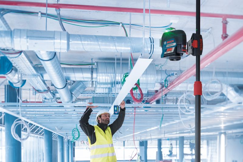 BT 350 안전 장비를 착용한 사람이 망원경 막대에 레이저 레벨링 도구를 사용하여 천장 패널을 설치하고 있습니다.