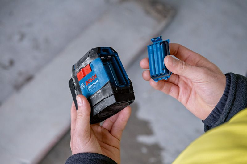 한 사람이 레이저 레벨링 도구를 잡고 빈 배터리 칸을 꺼내고 있습니다.