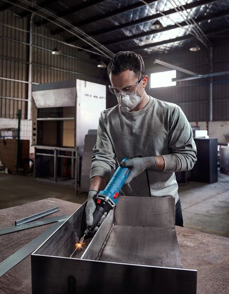 안전 장비를 착용한 사람이 산업 작업장 안에서 금속을 갈고 있습니다.