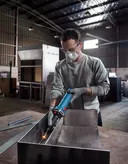 안전 장비를 착용한 사람이 산업 작업장 안에서 금속을 갈고 있습니다.