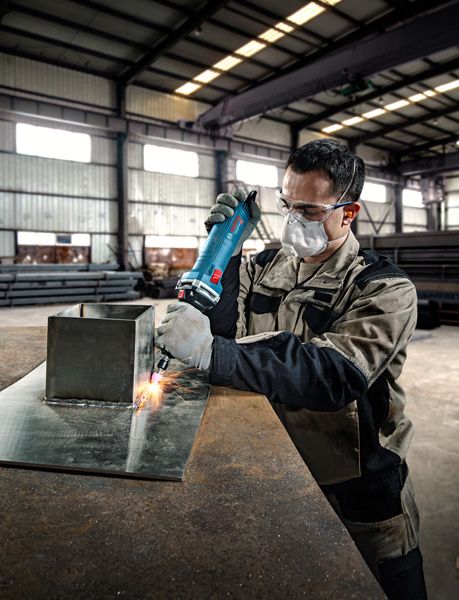 안전 장비를 착용한 사람이 금속판 위에서 직접 그라인더를 사용합니다.