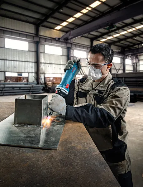 안전 장비를 착용한 사람이 금속판 위에서 직접 그라인더를 사용합니다.