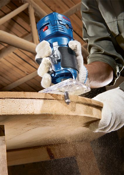 안전 장비를 착용한 사람이 휴대용 라우터로 나무를 다듬고 있고 톱밥이 날아다닌다.