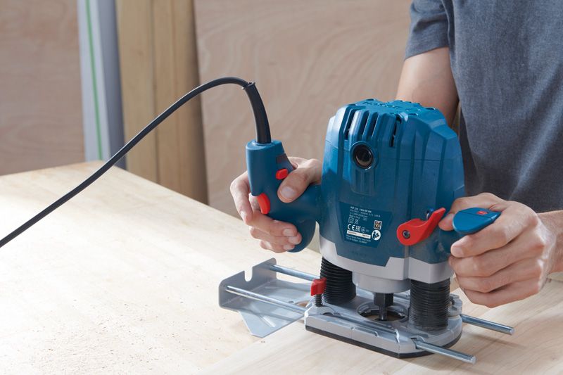 한 사람이 전기 라우터를 사용해 나무판의 가장자리 모양을 만들고 있습니다.