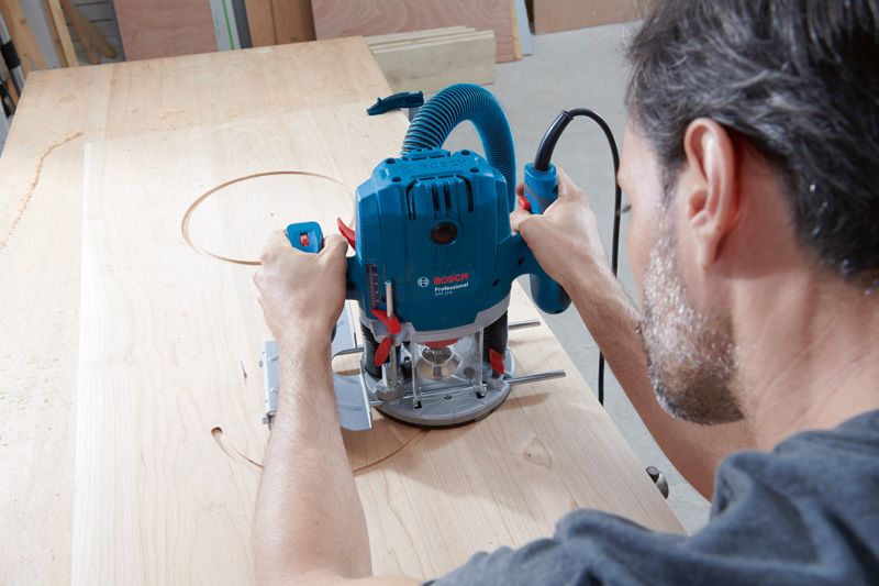 한 사람이 파란색 전기 라우터를 사용해 나무에 원형 패턴을 자릅니다.