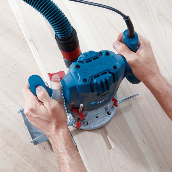 사람이 전기 라우터를 나무판을 따라 움직여 정밀한 홈을 절단합니다.