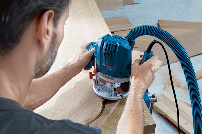 한 사람이 먼지 추출 기능이 있는 전동 라우터를 사용해 나무에 곡선 홈을 조각합니다.