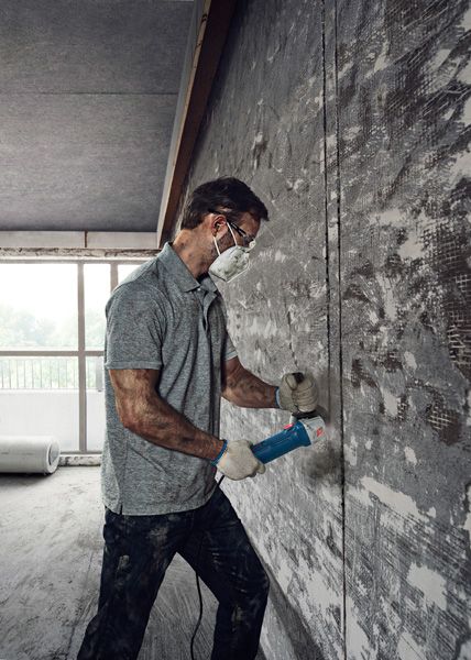 안전장비를 착용한 사람이 각도 그라인더를 사용해 콘크리트 벽을 자르고 있습니다.