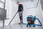 안전 장비를 착용한 사람이 무선 집진기를 사용하여 타일 바닥을 청소하고 있습니다.